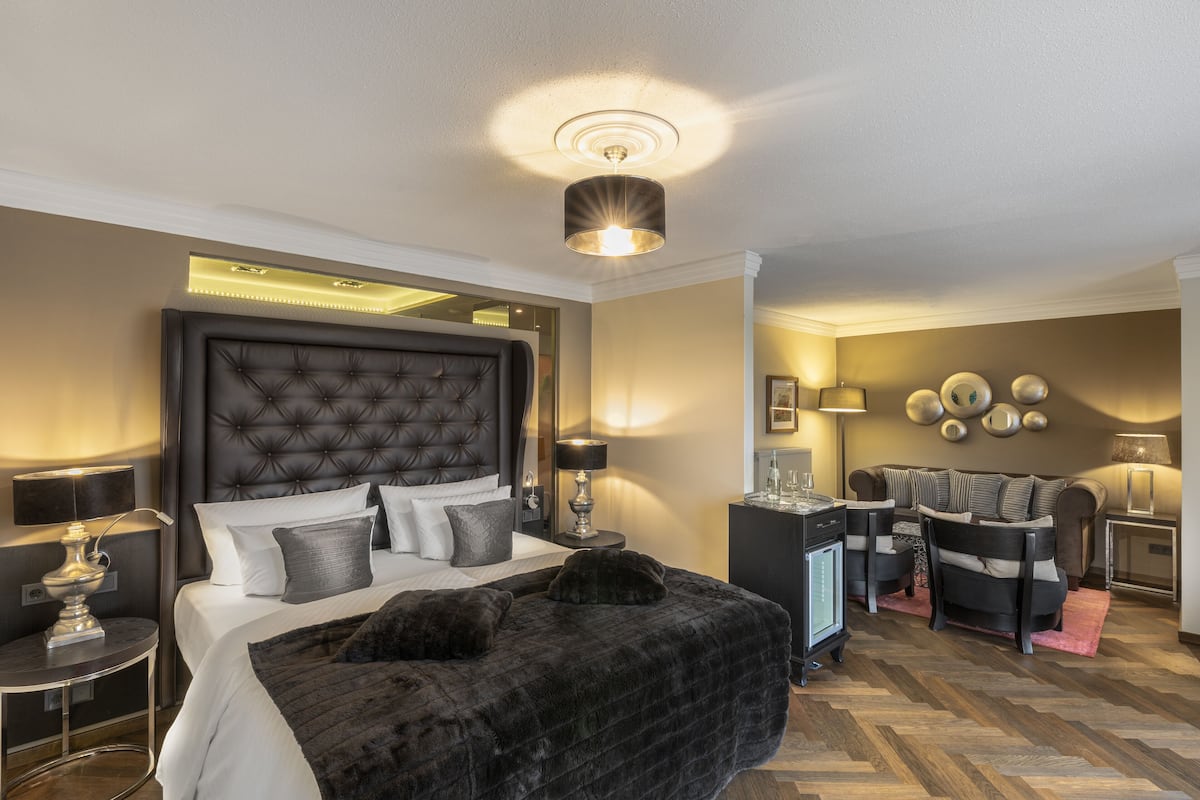 A hotel room with a large bed, a seating area with chairs, a desk, and a lamp.