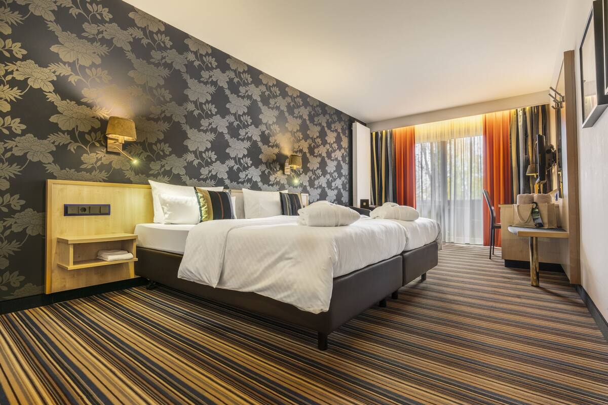 A hotel room with a large bed, a wooden headboard, a nightstand, and a desk with a chair.