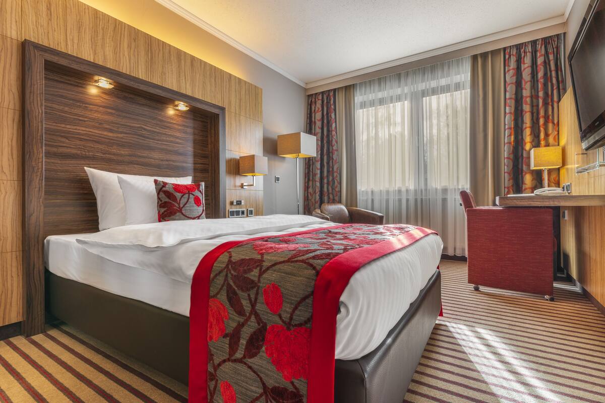 A hotel room with a large bed, a desk, a chair, and a TV.