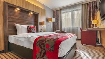 A hotel room with a large bed, a desk, a chair, and a TV.