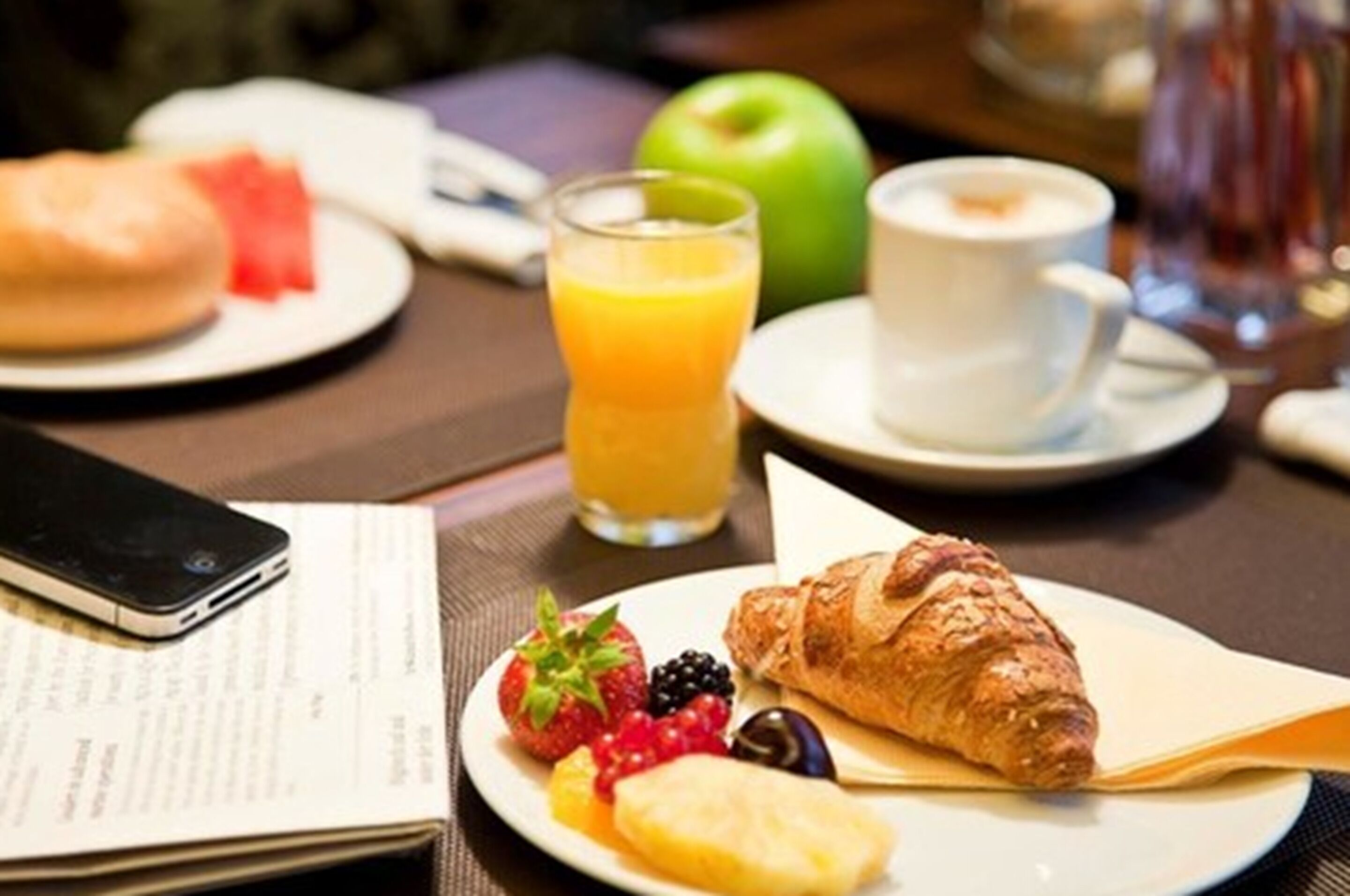 Esmorzar amb croissants, fruita, suc i cafè damunt d'una taula.