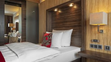 A hotel room with a large bed, a bedside table, a mirror, and a wall-mounted lamp.