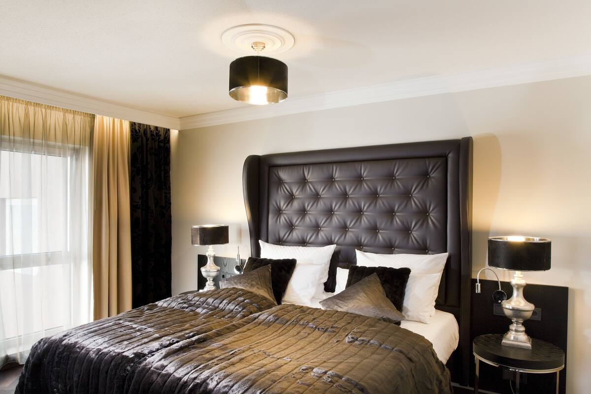 A hotel room with a large bed, a dark headboard, two bedside tables with lamps, and a window with curtains.