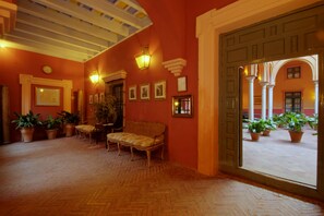 A hallway with a wooden floor, a bench, potted plants, and framed pictures on the walls. - Casa Palacio de Carmona (Carmona)