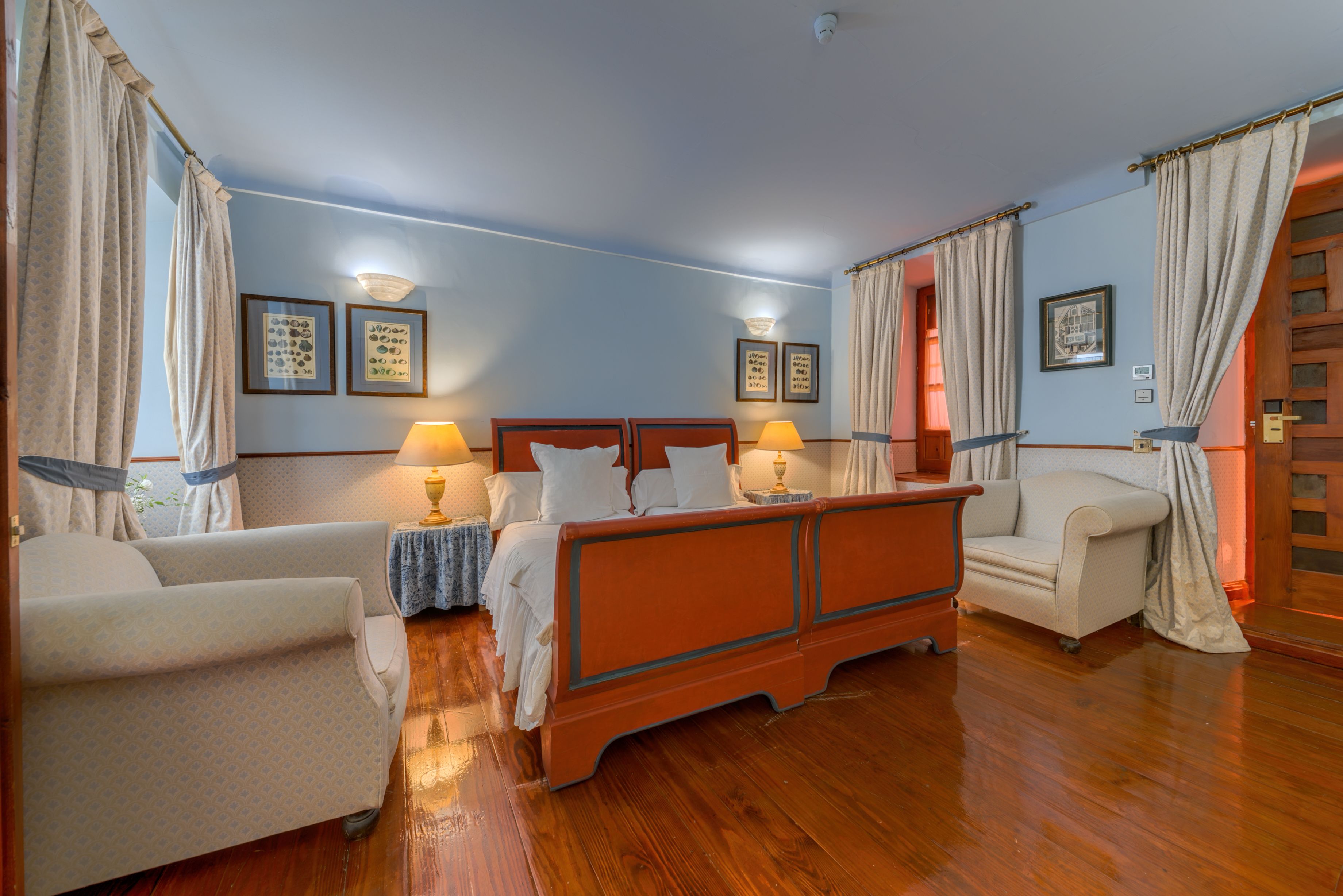 Una habitación de hotel con una cama de madera, dos mesitas de noche con lámparas, un sofá y una silla.