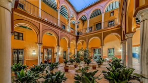 Um pátio amplo com várias arcadas, plantas em vasos e uma fonte central.