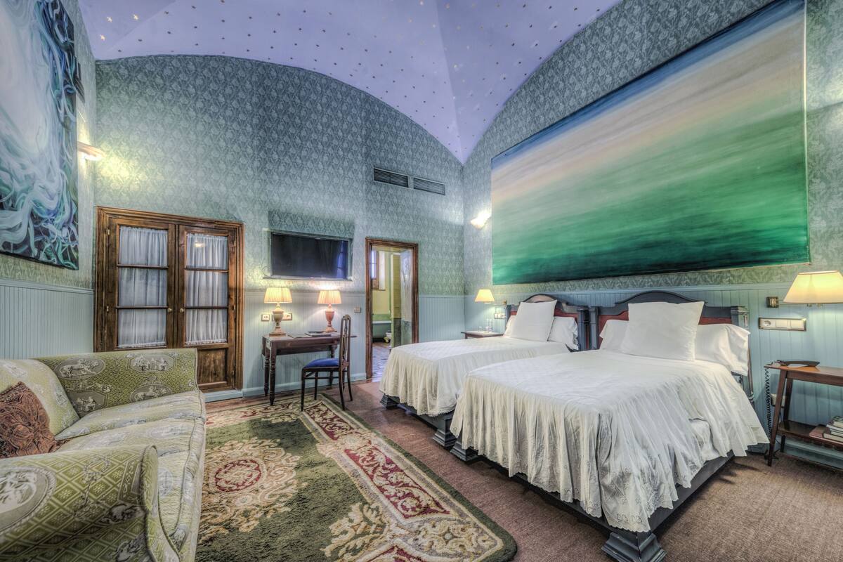 Habitación de hotel con dos camas, un sofá, un escritorio y un cuadro grande en la pared.