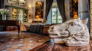 Um quarto com uma mesa de madeira, uma grande escultura de cabeça de cavalo, um armário verde com portas de vidro e uma janela com cortinas.