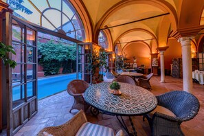 A spacious patio area with round tables and wicker chairs, large windows, and a view of a pool. - Casa Palacio de Carmona (Carmona)