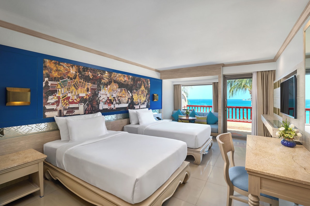 Une chambre d’hôtel avec deux lits, un bureau, une chaise, une télévision et un grand tableau au mur.