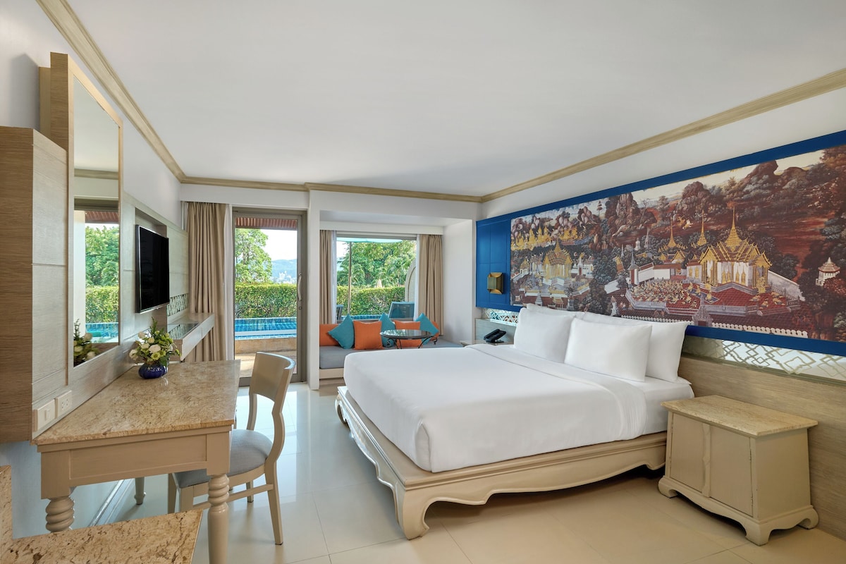 Une chambre d’hôtel avec un lit, un bureau, une chaise, une petite table et une grande fresque murale.