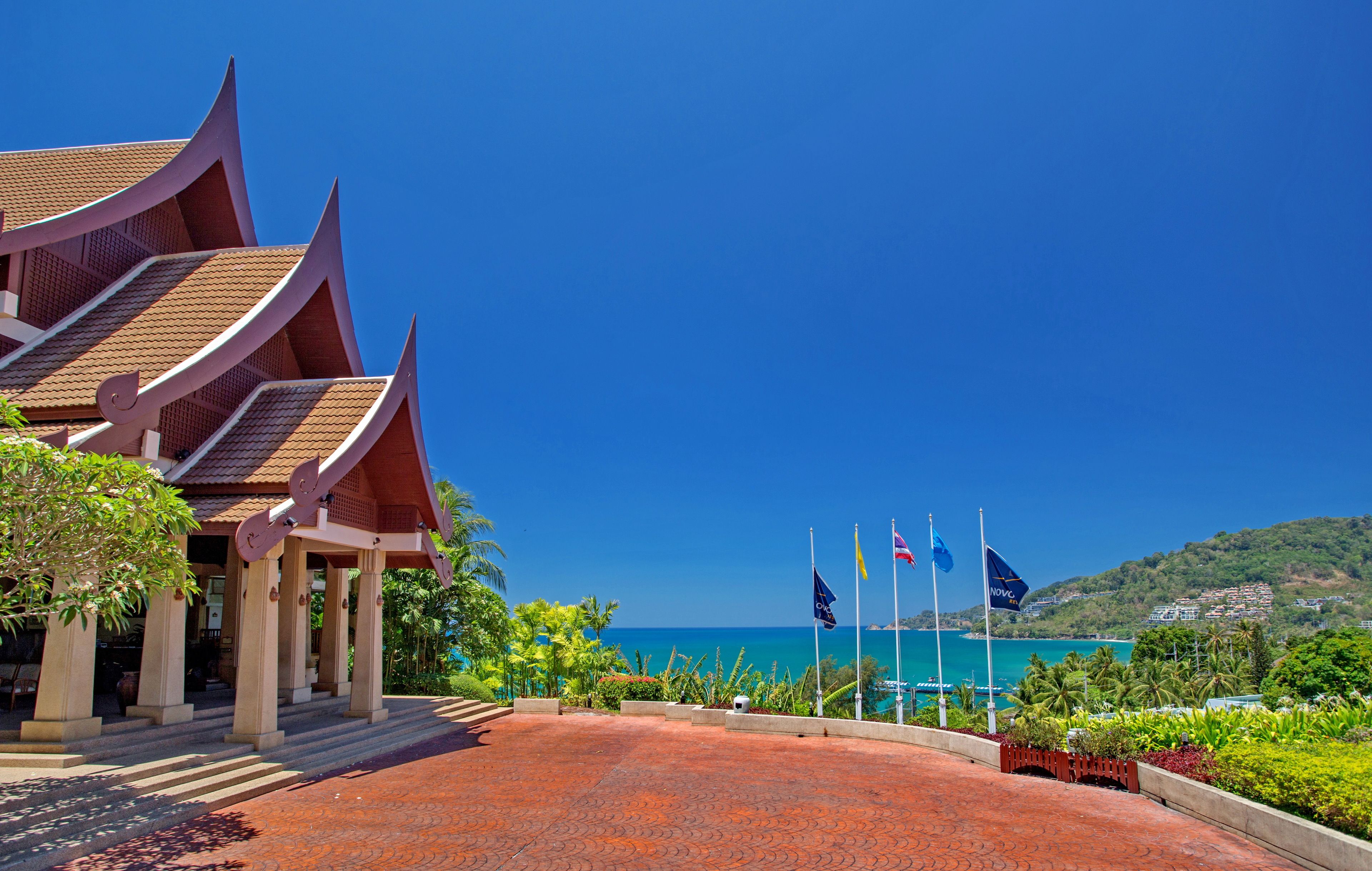 A traditional Thai building with a curved roof, a paved entrance, and a view of the ocean.