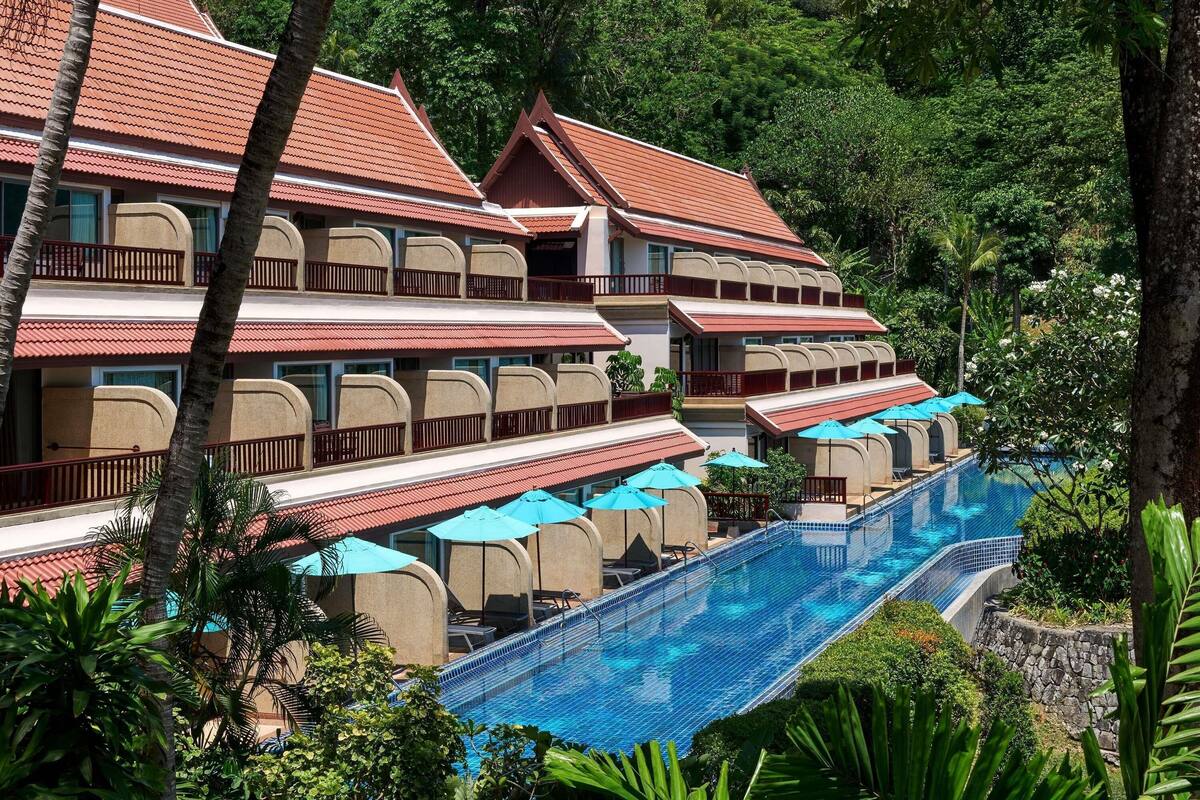 A resort with multiple-story buildings, a swimming pool, and lush greenery.