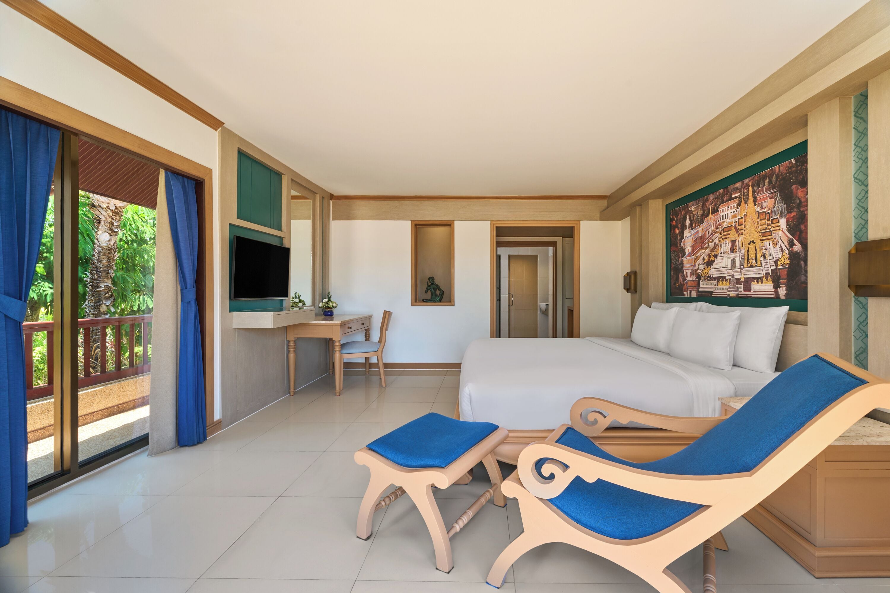 Habitación de hotel con cama, escritorio, televisor, balcón con cortinas y un cuadro en la pared.