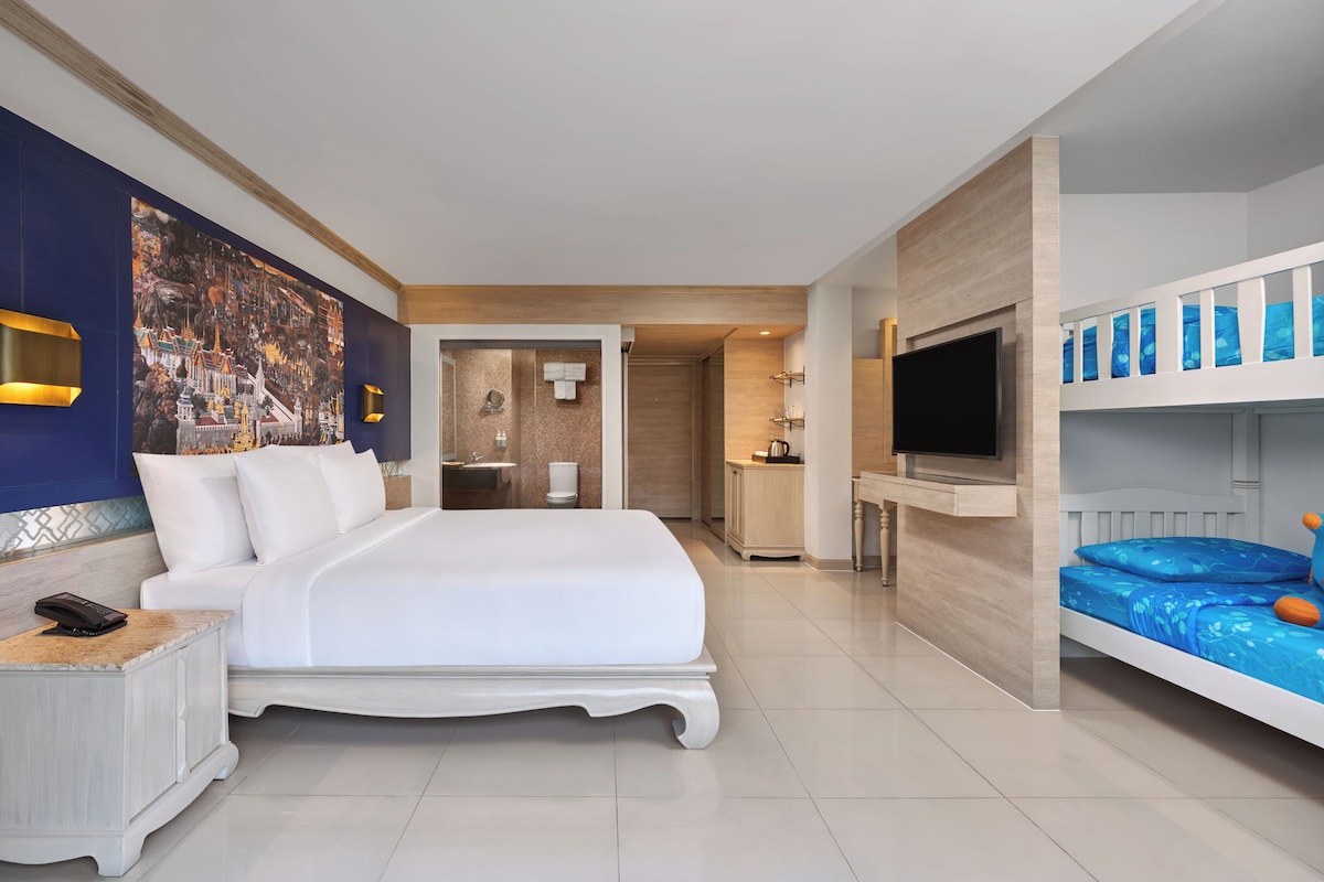Une chambre d’hôtel avec un grand lit, une télévision, un lit superposé, une salle de bain et un coin cuisine.