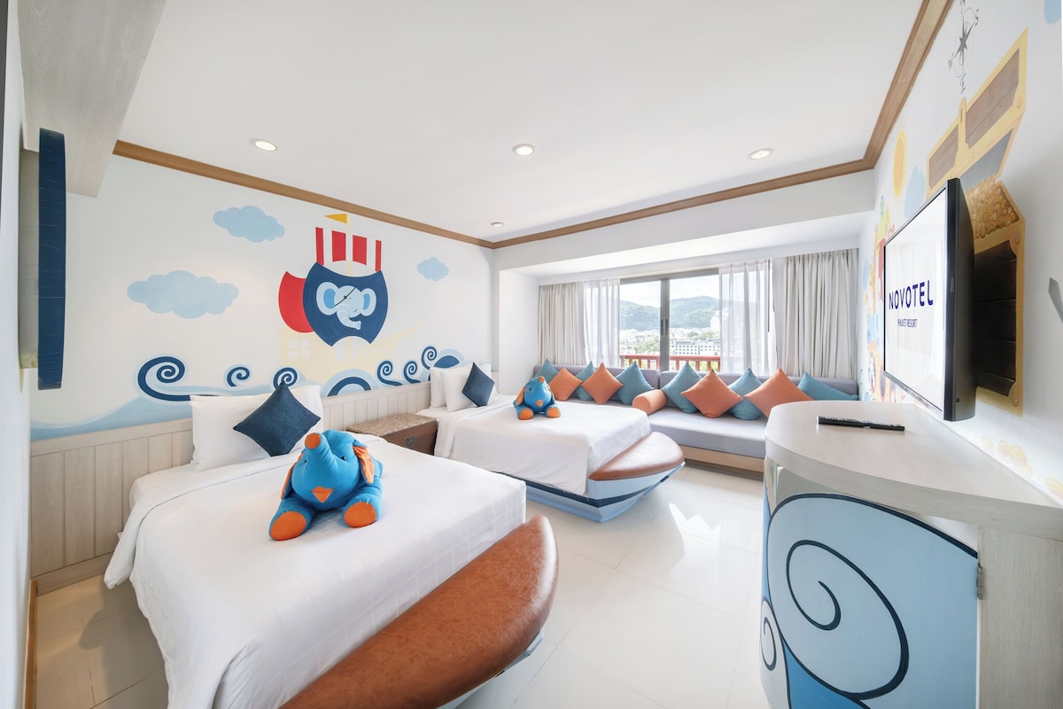 Une chambre d’hôtel avec deux lits, un canapé-lit, une télévision et une fresque murale.