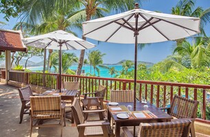 An outdoor seating area with wicker furniture, white umbrellas, and a view of the ocean.