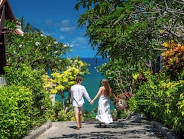 A couple walking down a tree-lined path with a view of the ocean.