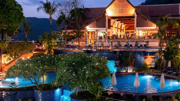 A resort with a swimming pool, a waterfall, and a building with a distinctive roof.