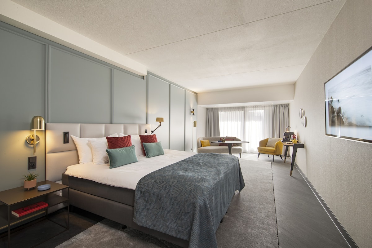 A modern hotel room with a large bed, bedside tables, a desk, and a chair.