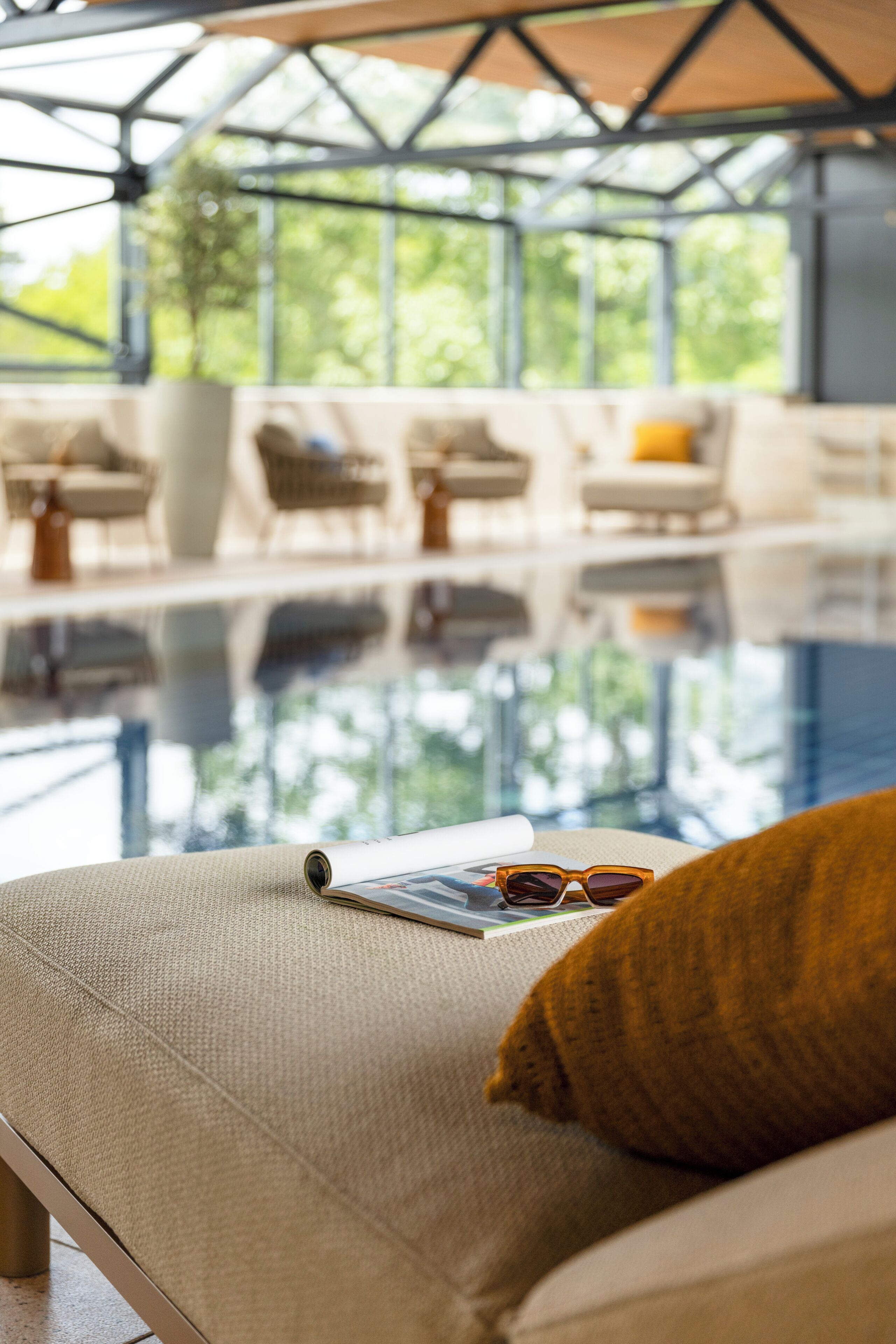 Un área de descanso junto a la piscina, con piscina cubierta por cristal, sillones de baño y un sofá con cojín.