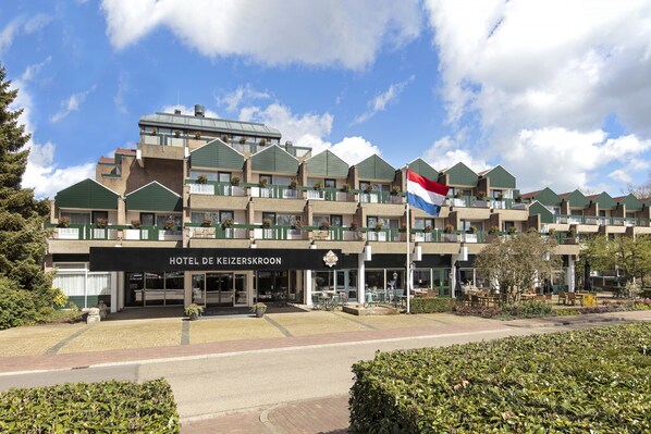 A hotel with multiple balconies, a flag, and a well-maintained garden. - Bilderberg Hotel De Keizerskroon (Apeldoorn)