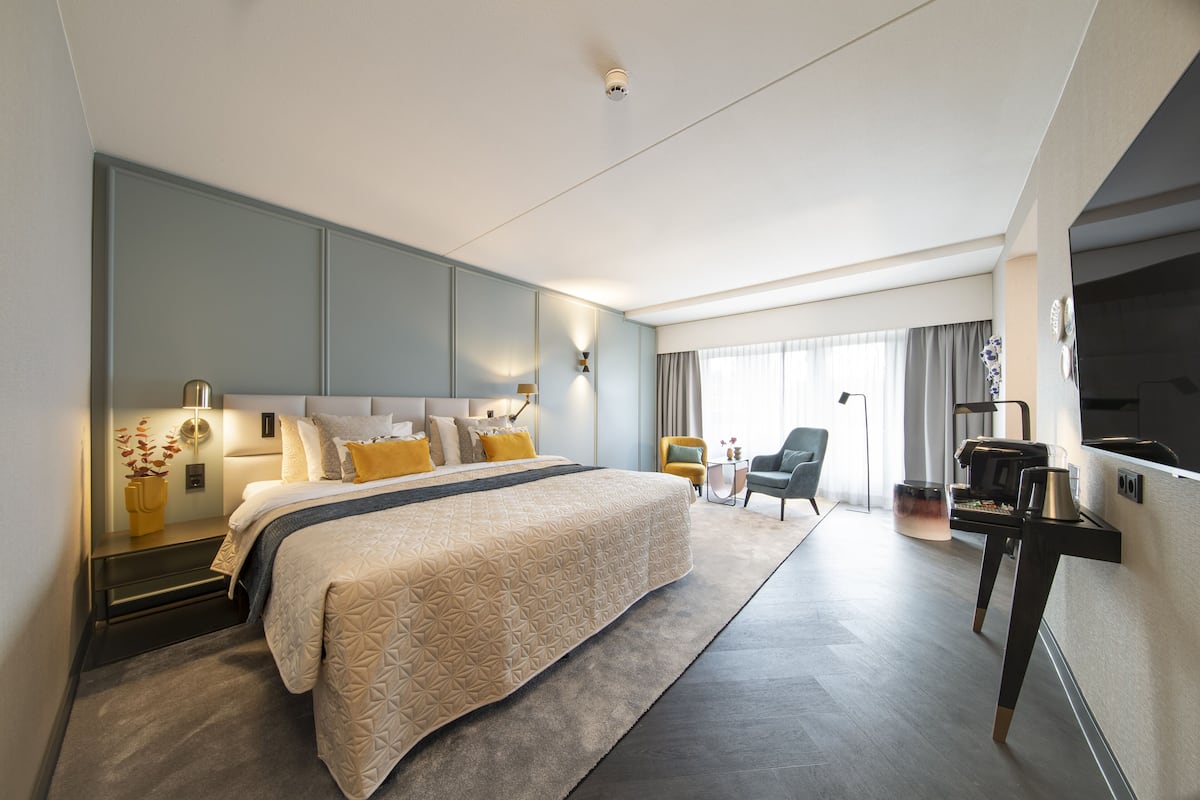 A modern hotel room with a large bed, bedside tables, a desk, and a seating area.