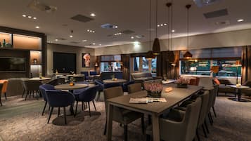 Un hall d’hôtel moderne doté d’un espace repas, de différents coins salon et de grandes fenêtres offrant une vue sur l’extérieur.