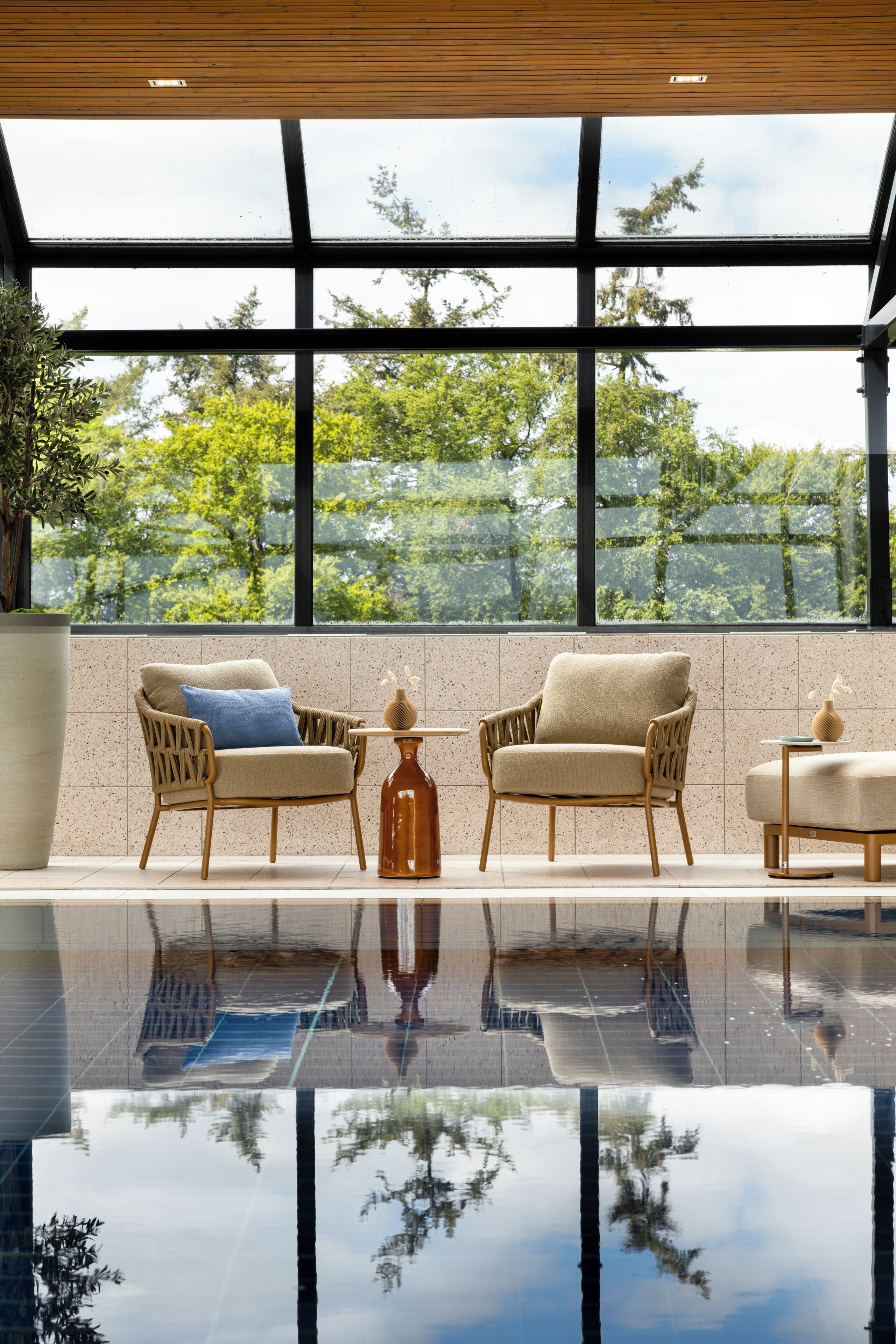 A modern interior with a glass ceiling, two wicker armchairs, a small table, and a potted plant.