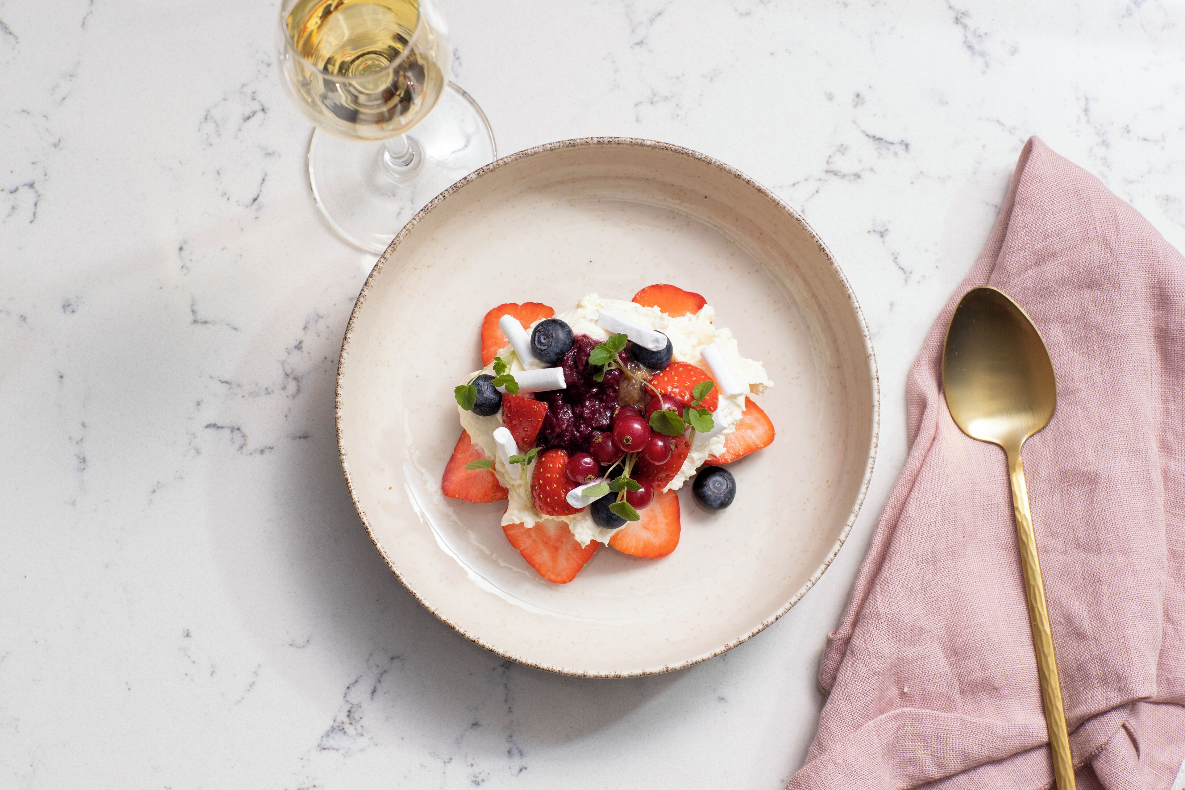 Ein Dessertteller mit Erdbeeren, Blaubeeren und Sahne auf einer Marmorplatte.