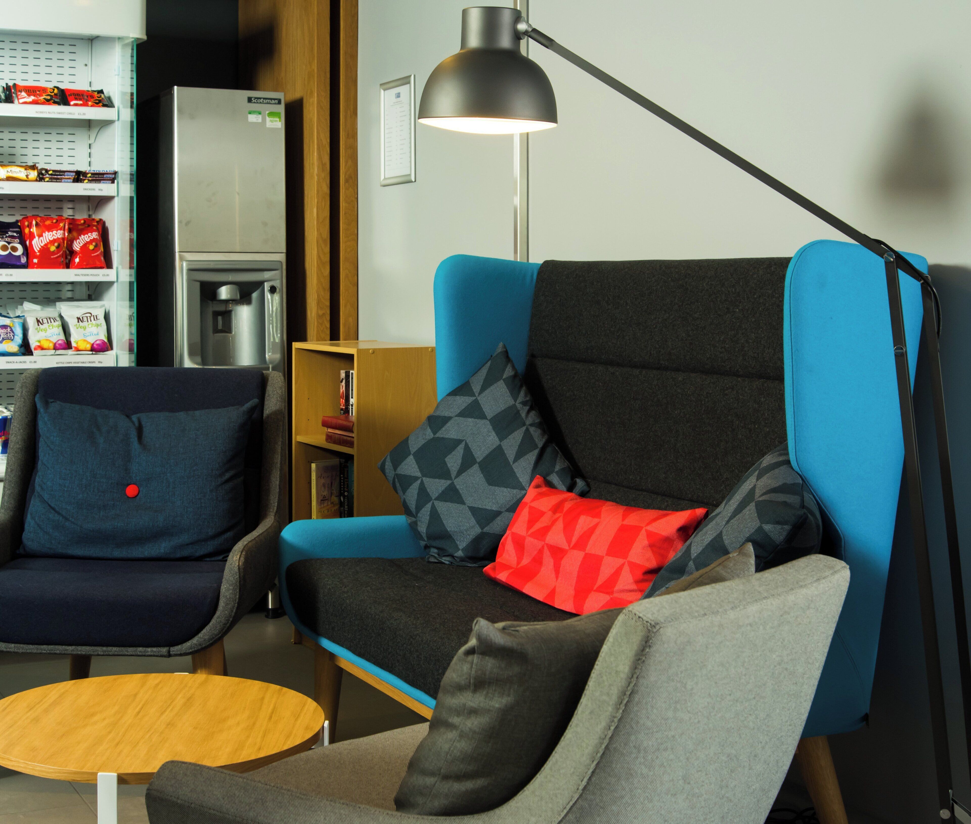 A modern living room with a blue armchair, a smaller chair, a round wooden table, and a floor lamp.
