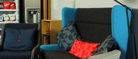 A modern living room with a blue armchair, a smaller chair, a round wooden table, and a floor lamp.