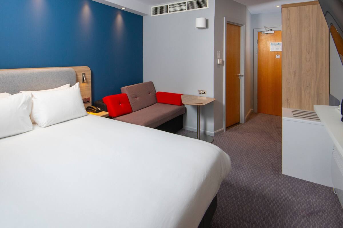 A hotel room with a large bed, a sofa, a small table, and a desk.