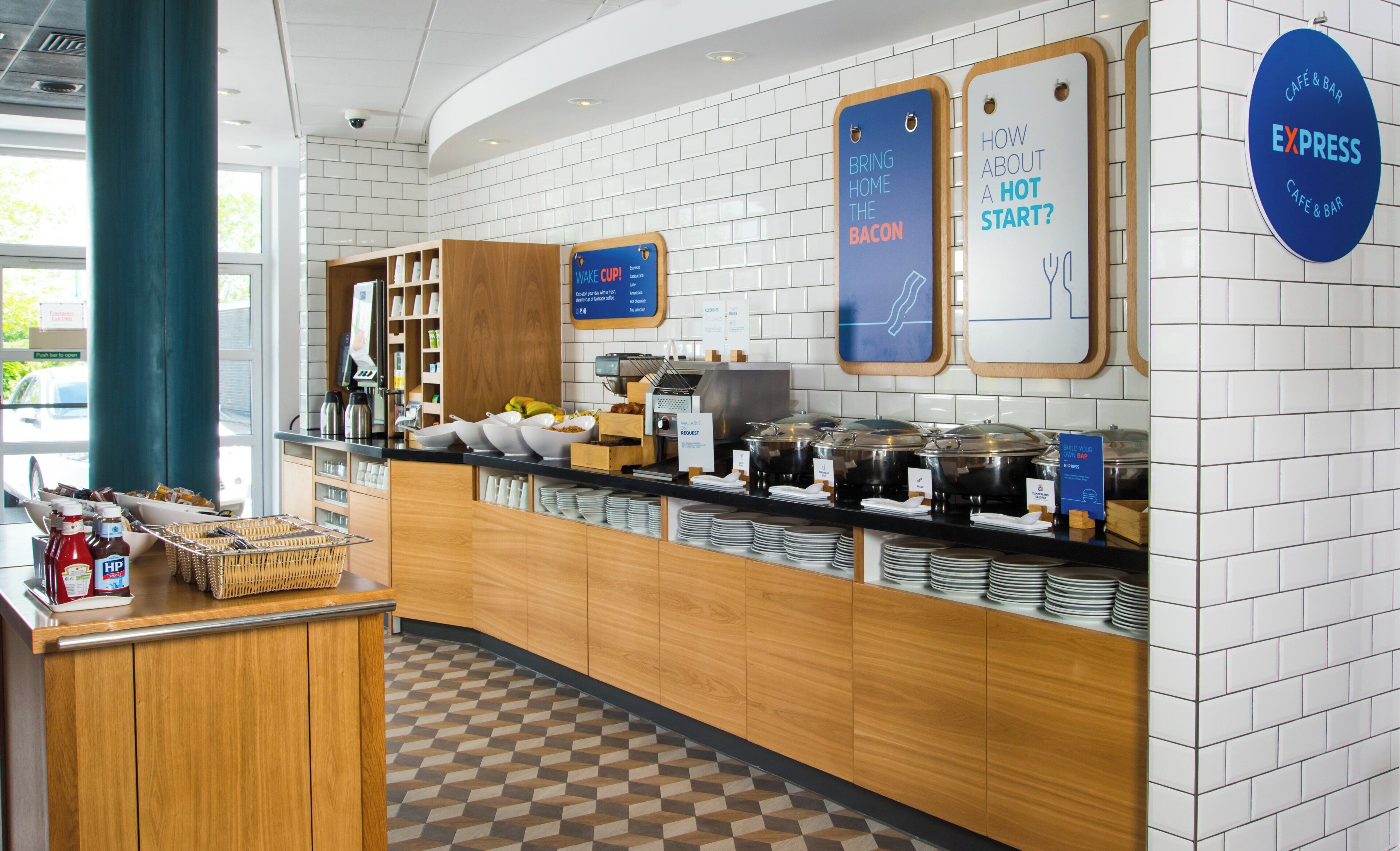 A breakfast buffet area with various food options, a coffee station, and informational signs.