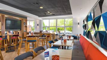 A modern restaurant with wooden furniture, a flat-screen TV, and large windows offering a view of the outdoors.