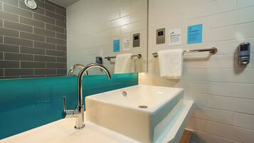 A modern bathroom with a white sink, a chrome faucet, and a teal-colored bathtub. There are towels hanging on a rack and a sign on the wall.
