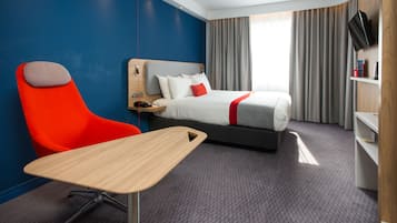 A hotel room with a bed, a desk, a chair, a TV, and a shelf with toiletries.