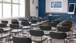 A conference room with rows of grey chairs, a projector screen with a Holiday Inn Express logo, and a clock on the wall. - Holiday Inn Express Burton Upon Trent by IHG (Burton on Trent)