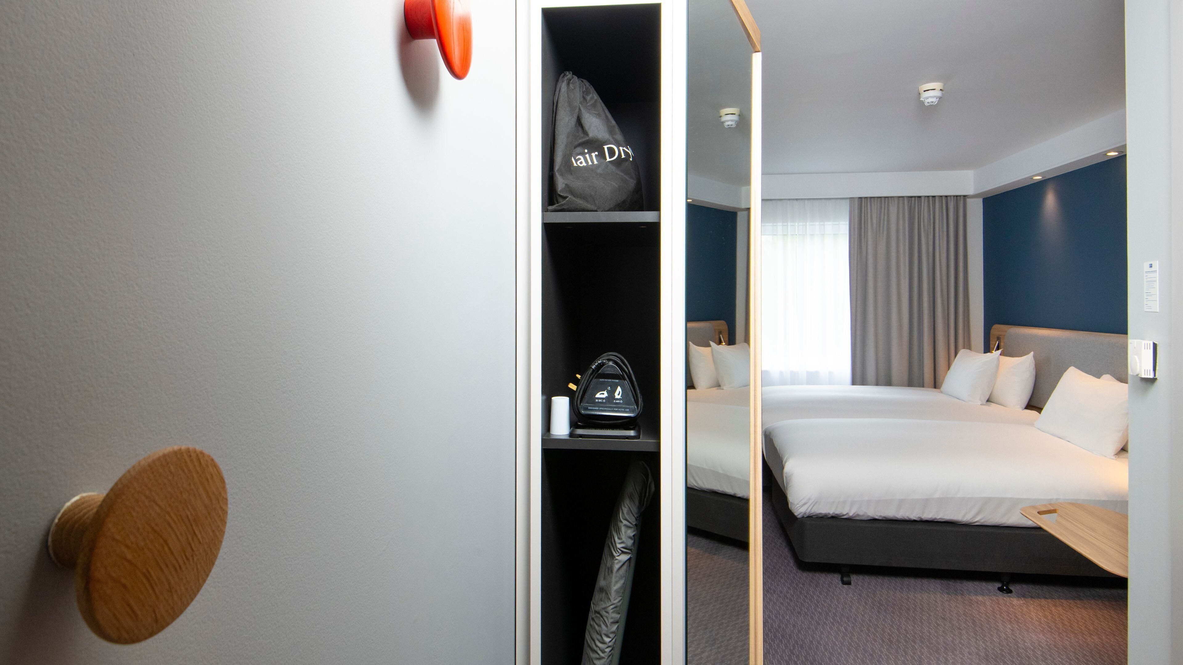 A hotel room with a bed, a wardrobe, a hair dryer, and a thermostat.