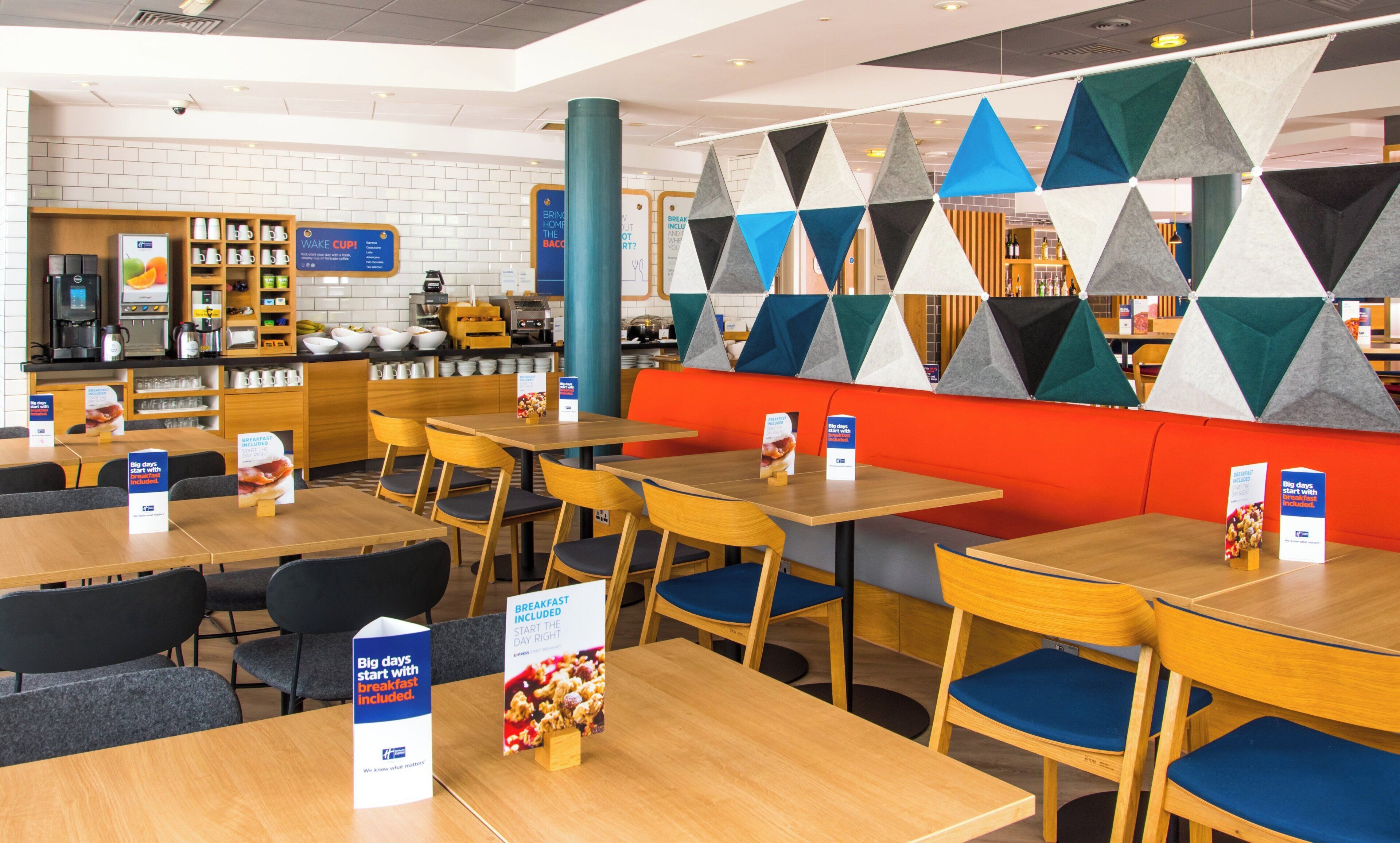 A modern cafe with wooden tables and chairs, a breakfast menu, and a colorful geometric wall design.