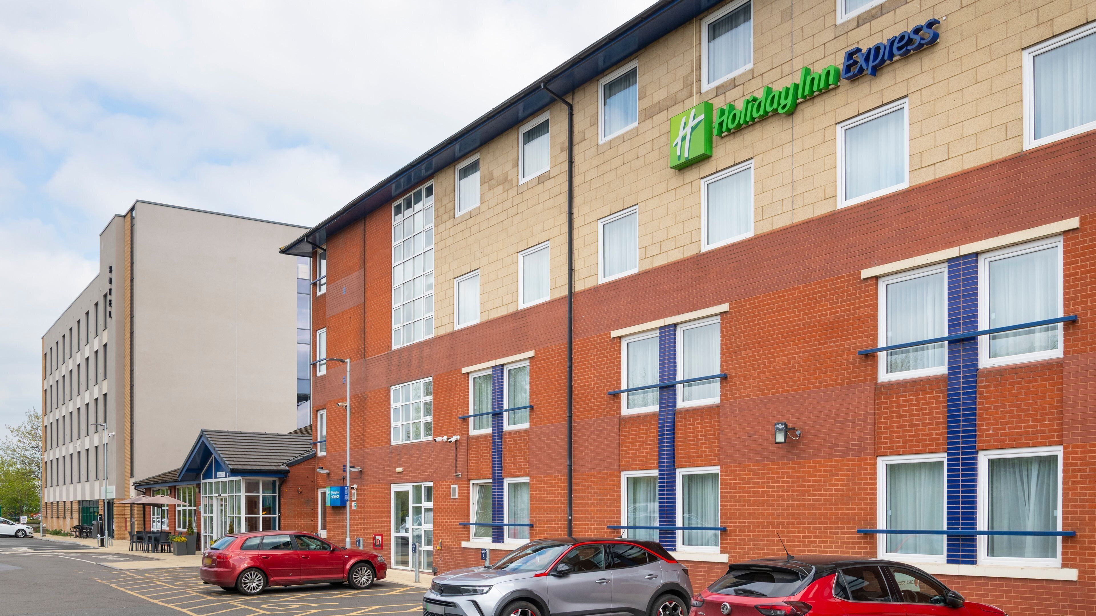 A Holiday Inn Express building with a brick facade, multiple windows, and a parking lot with several cars.
