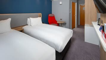Een hotelkamer met twee bedden, een rode stoel, een bureau en een deur naar een badkamer.