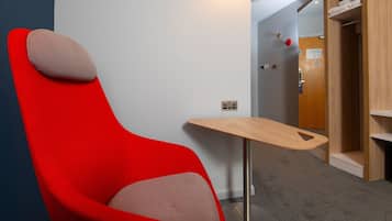 Una camera moderna con una sedia rossa, un piccolo tavolo in legno e una porta che dà su un bagno.
