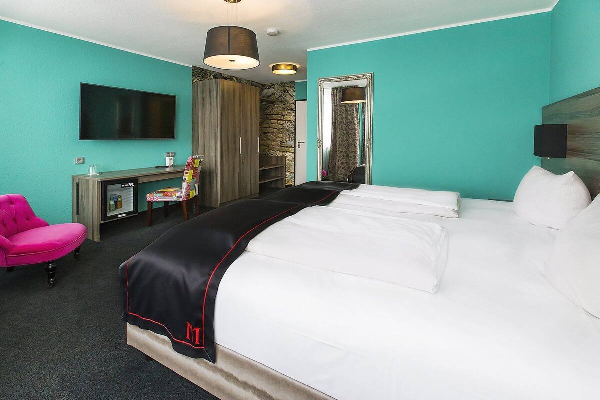 Une chambre d’hôtel avec un grand lit, un bureau avec un ordinateur, une chaise et un téléviseur fixé au mur.