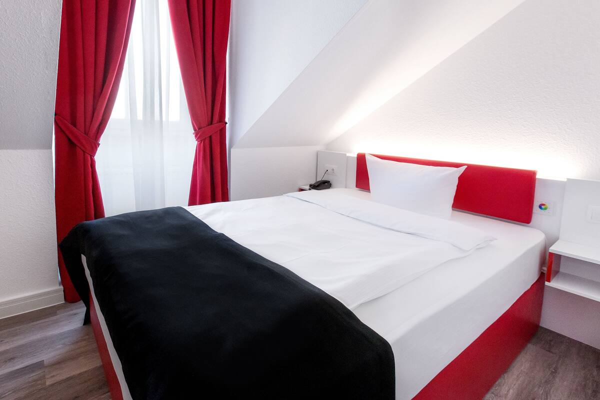 Une chambre d’hôtel moderne avec un lit, des rideaux rouges et un mur blanc.