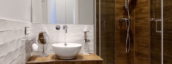 Un baño moderno con un lavabo blanco tipo recipiente, un espejo de mano y un vaso de agua sobre el mostrador.