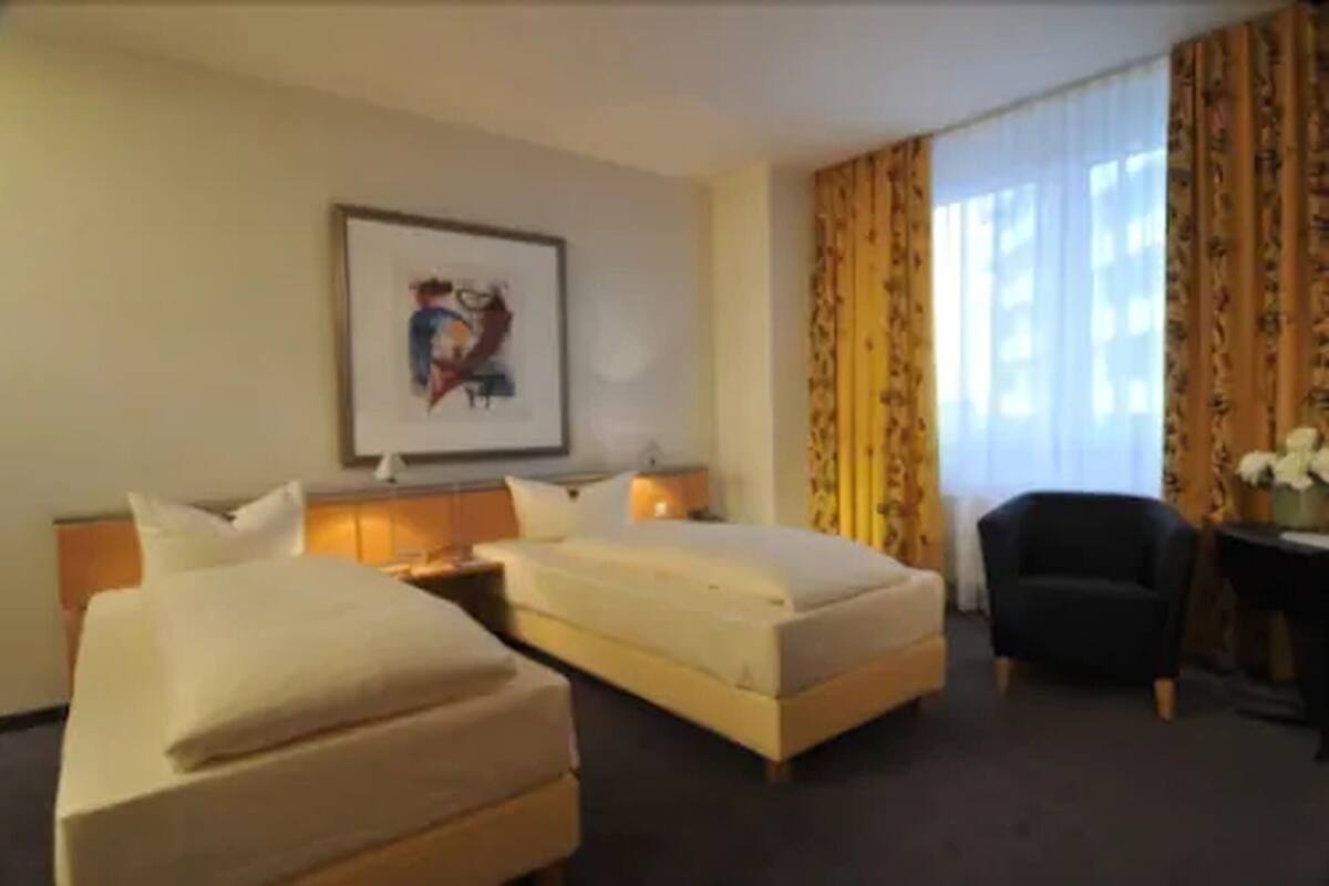 A hotel room with two beds, a desk, a chair, and a framed picture on the wall.