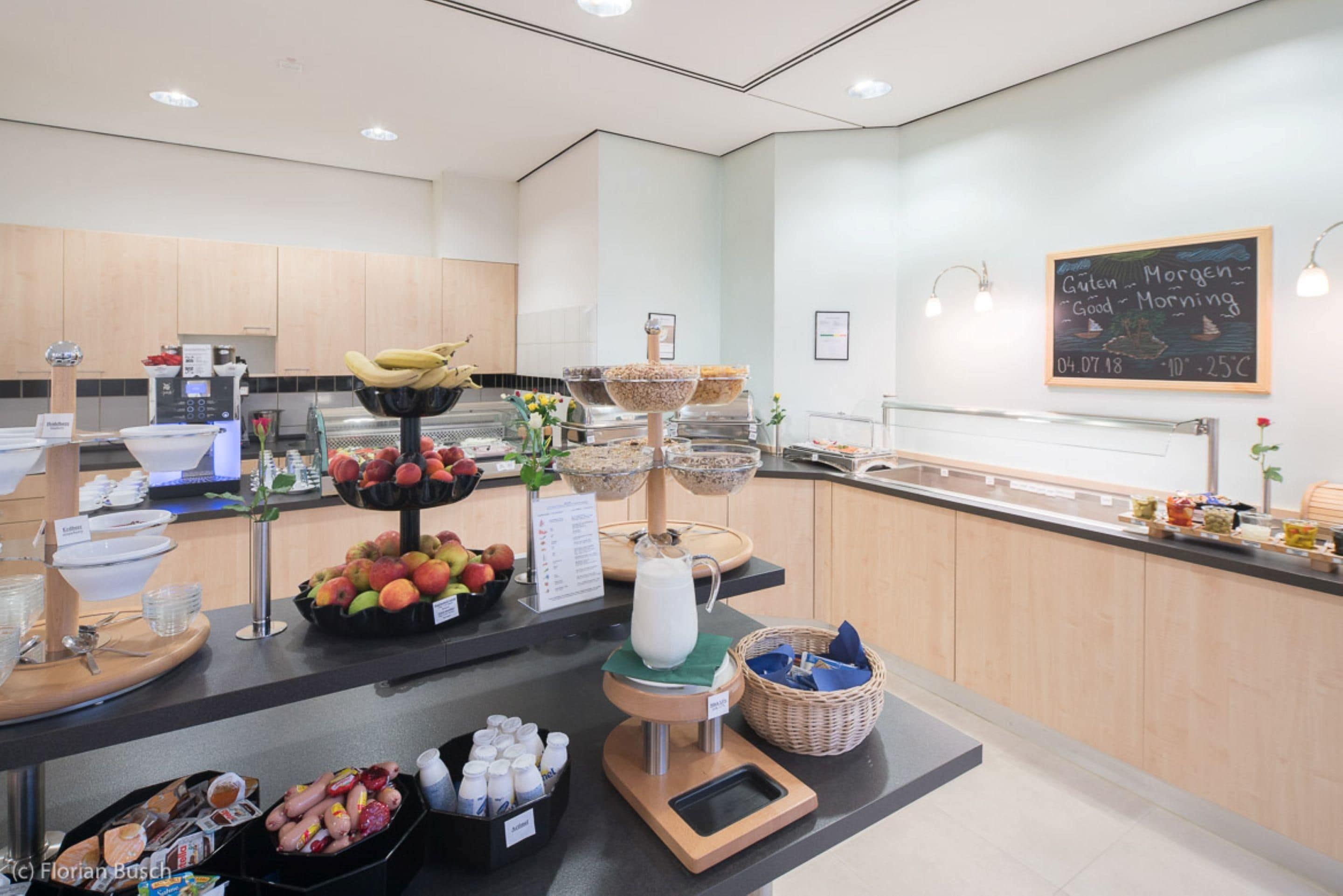 A breakfast buffet with various fruits, a milk dispenser, and a chalkboard with a message.