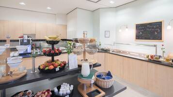 A breakfast buffet with various fruits, a milk dispenser, and a chalkboard with a message.