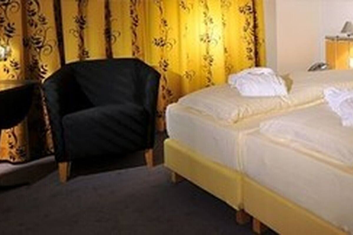A double bed with white linens, a bedside table with a lamp, and a chair.